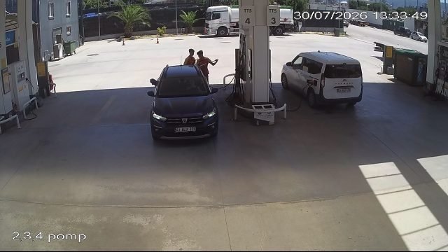 Car at a dispenser with two people at the pump, plate redacted